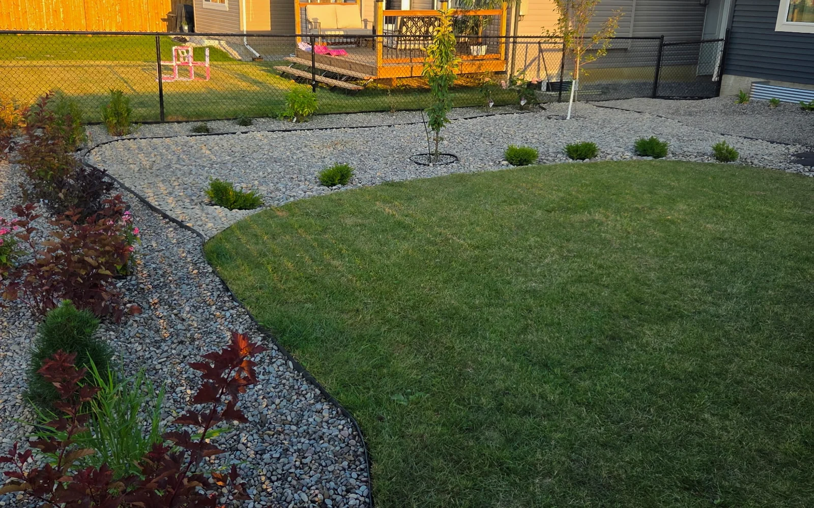 Finished full-property landscape installation with curved rock beds, lawn, trees and shrubs